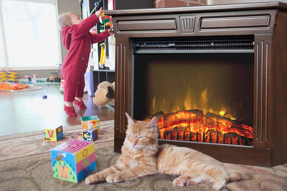 Cat resting near an Amish Fireplace with a toddler playing in the background