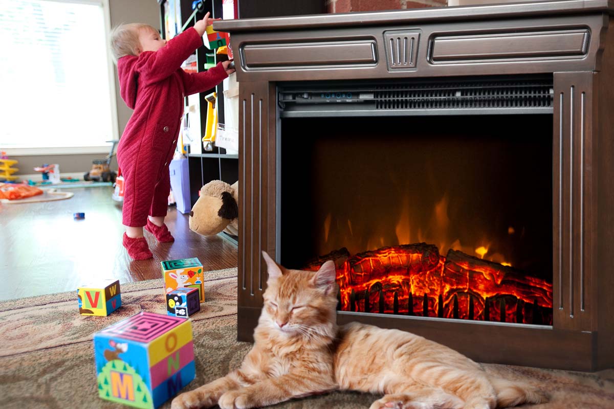 Cat resting near a Heat-n-Glow with a toddler playing in the background